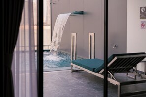 Une piscine intérieure moderne agrémentée d’une cascade, d’un fauteuil de relaxation et offrant une vue sur de hauts immeubles.