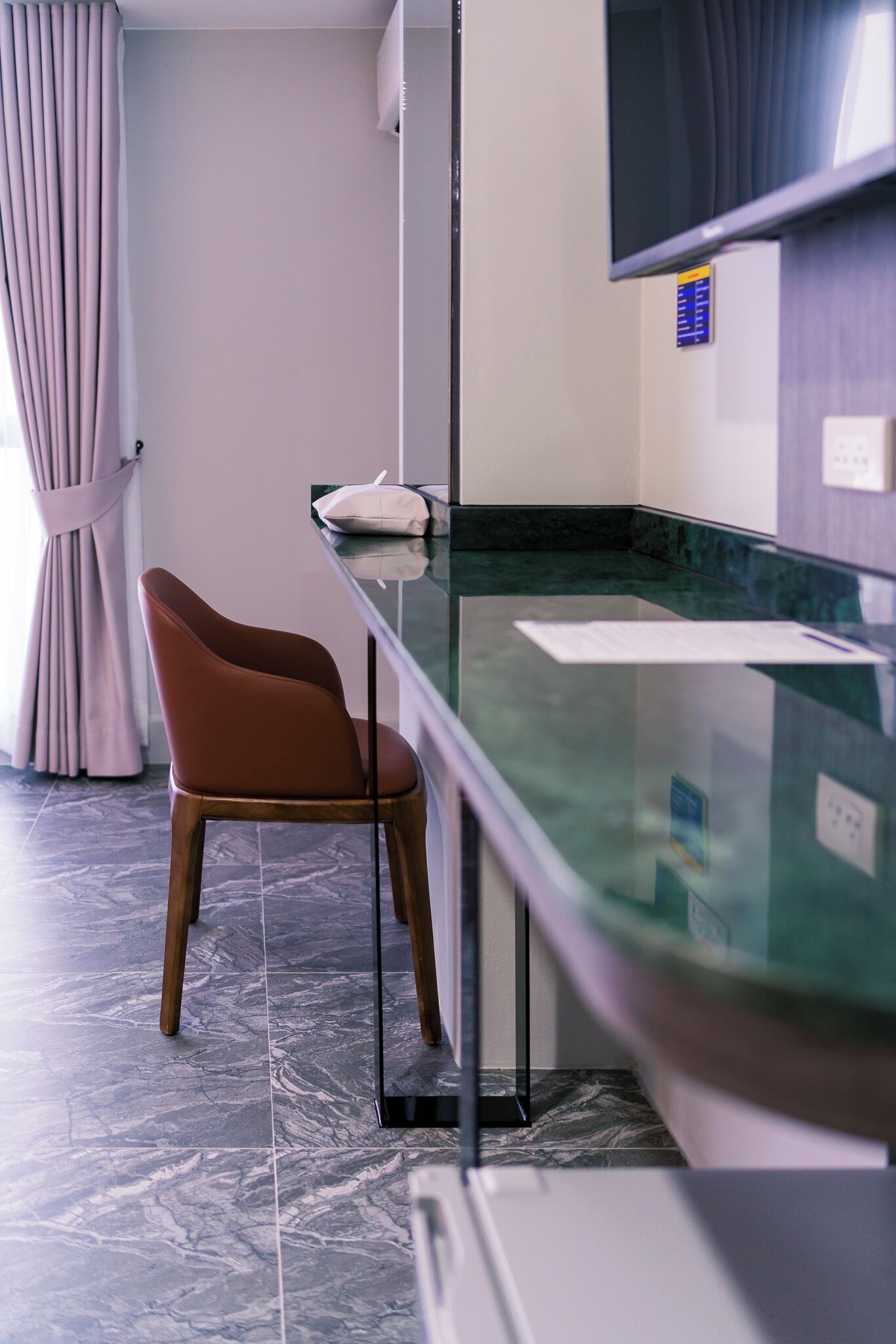 Habitación moderna con separador de vidrio, una silla marrón, almohada blanca y televisor de pantalla plana montado en la pared.
