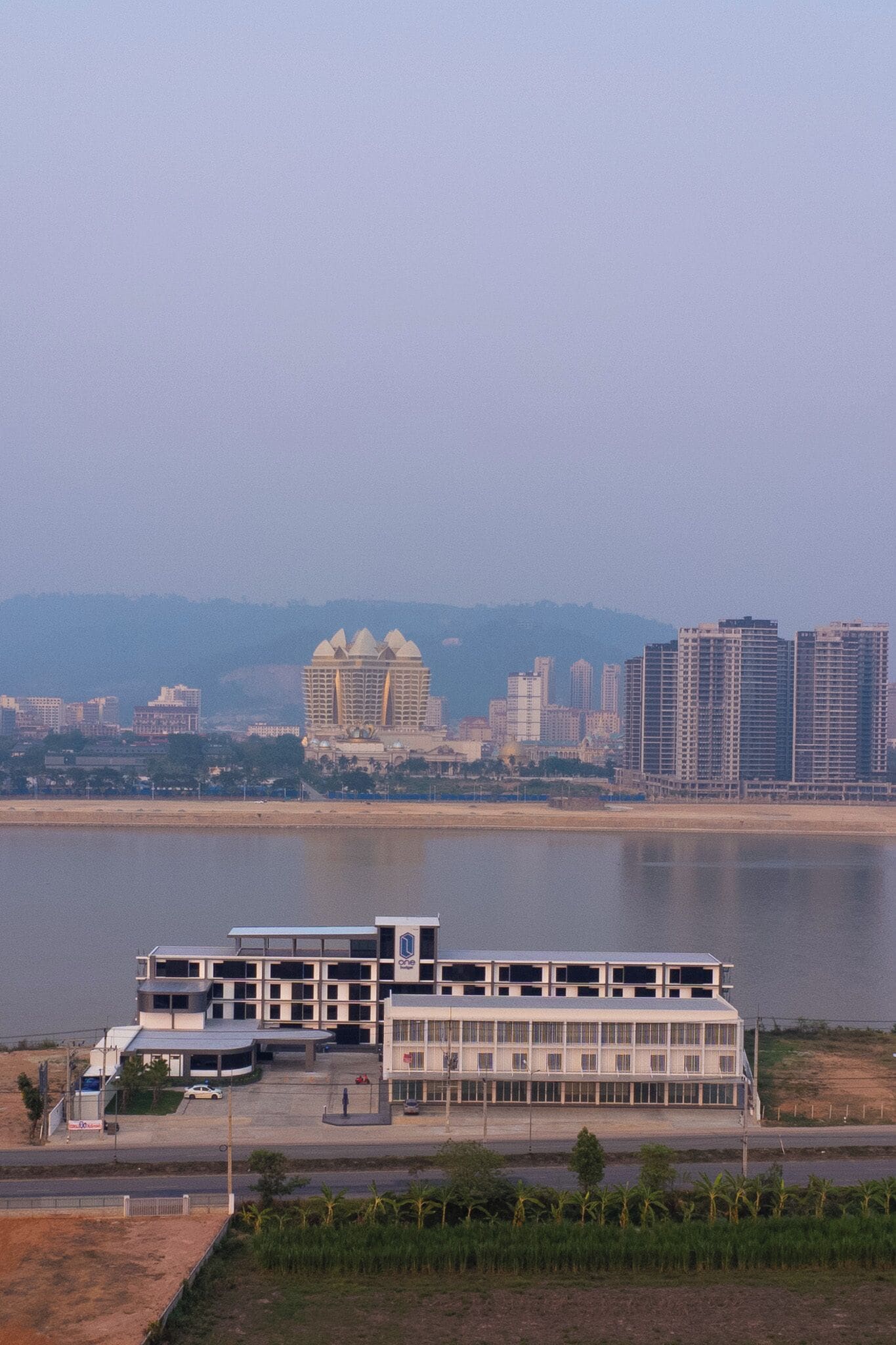 Un bâtiment moderne à plusieurs étages, doté d’un espace de stationnement et bordé, à l’arrière-plan, par un plan d’eau.