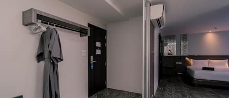 Habitación de hotel con cama, bata colgada en un perchero, una puerta y un aire acondicionado instalado en la pared.