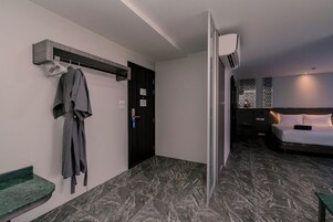 Habitación de hotel con cama, bata colgada en un perchero, una puerta y un aire acondicionado instalado en la pared.