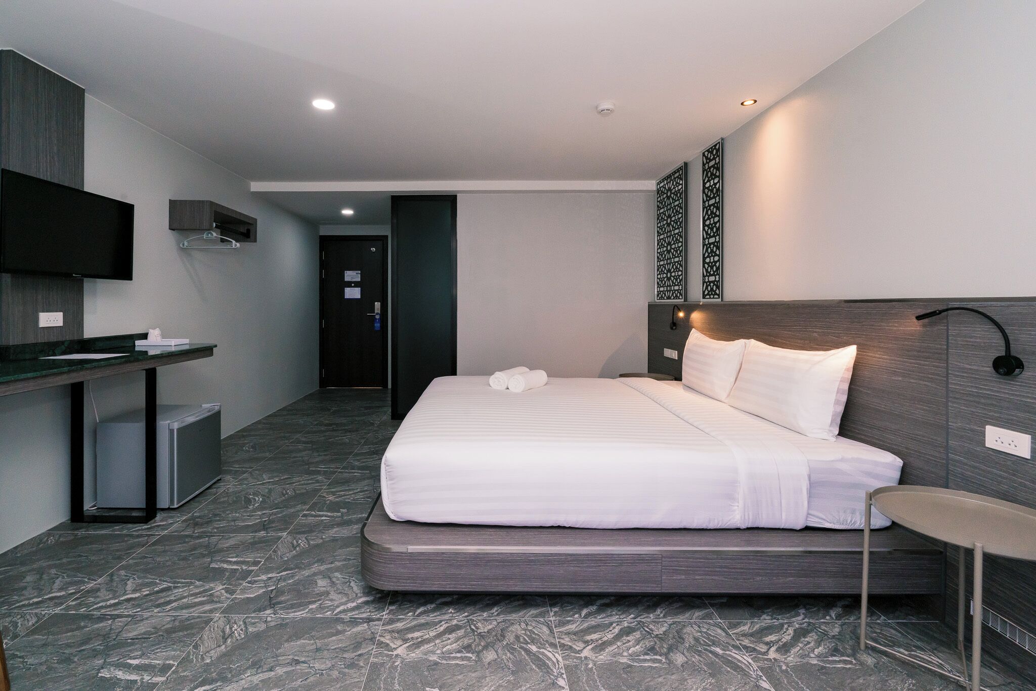 Quarto de hotel com cama, mesa de cabeceira e escrivaninha com televisão de tela plana.