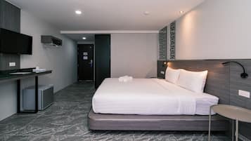 Quarto de hotel com cama, mesa de cabeceira e escrivaninha com televisão de tela plana.