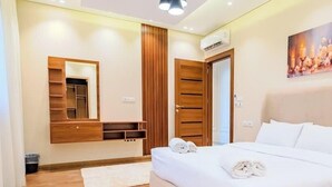 A bedroom with a bed, a wooden wardrobe, a mirror, and a painting on the wall. - Luxury 3BR • Lakeview Residence • Premium Stay (القاهرة)