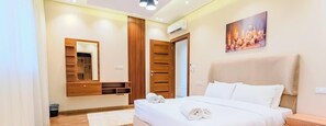 A bedroom with a bed, a wooden wardrobe, a mirror, and a painting on the wall. - Luxury 3BR • Lakeview Residence • Premium Stay (القاهرة)