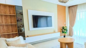 A modern living room with a flat-screen TV, a round wooden coffee table, and a large window with sheer curtains. - Luxury 3BR • Lakeview Residence • Premium Stay (القاهرة)