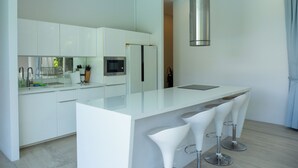 Una cocina moderna con armarios blancos, una campana extractora de acero inoxidable, horno empotrado y una isla grande con taburetes de bar.