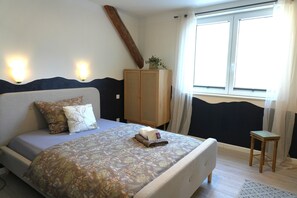 A bedroom with a bed, bedside table, lamp, window, and a wooden cabinet. - Haevn by the Sea, Water Room (Reußenköge)