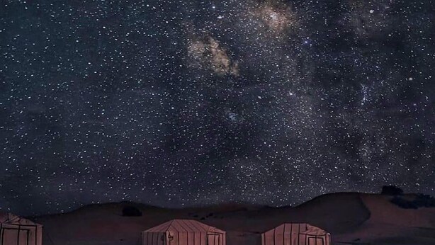 A starry night sky with a campfire and yurts in a desert setting. - Desert Luxury Camp (Merzouga)
