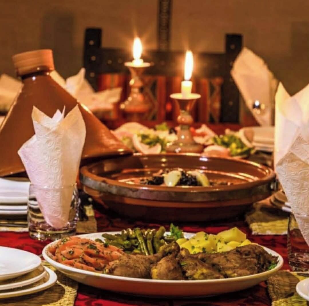 A dining table with a variety of dishes, a traditional Moroccan tagine, and a candle.