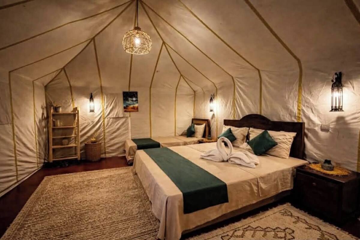 Un hébergement sous tente comprenant un lit, des lampes de chevet, une étagère et un tapis.