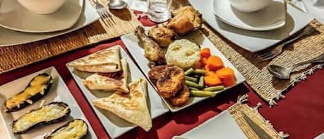 Mesa dispuesta con diversos platos, incluyendo pollo asado, verduras y pan, acompañada de tazas de café.