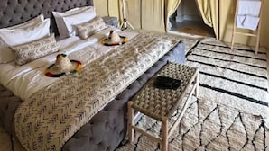 A tented room with a bed, a small table, and a hanging light fixture. - Desert Luxury Camp (Merzouga)