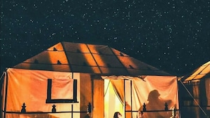 A tent with a window and a door, a person sitting inside, and a person standing outside. - Desert Luxury Camp (Merzouga)