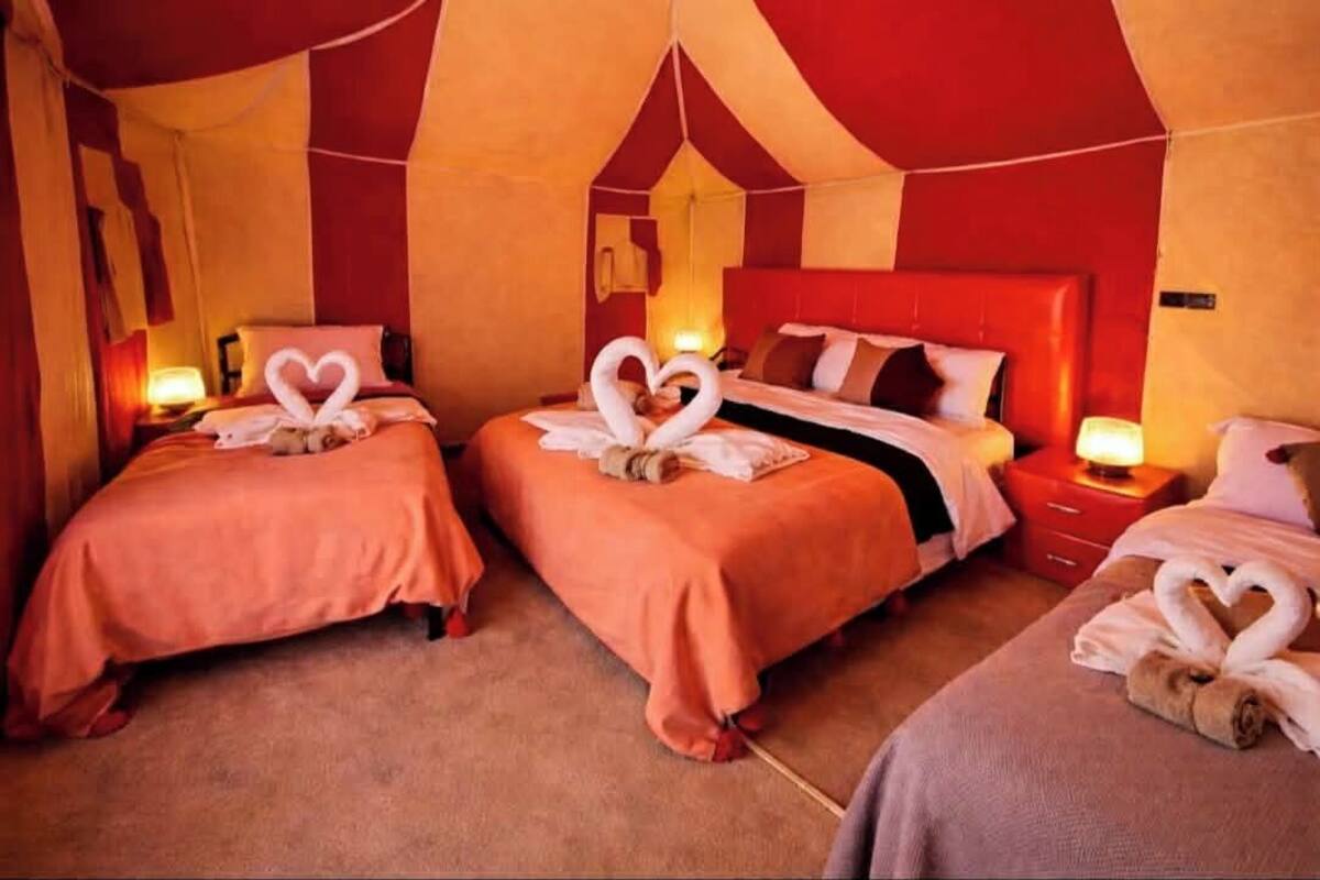 Une chambre d’hôtel avec deux lits, chacun agrémenté d’une décoration en forme de cœur faite avec des serviettes, des murs rouges et beige, et des lampes de chevet.