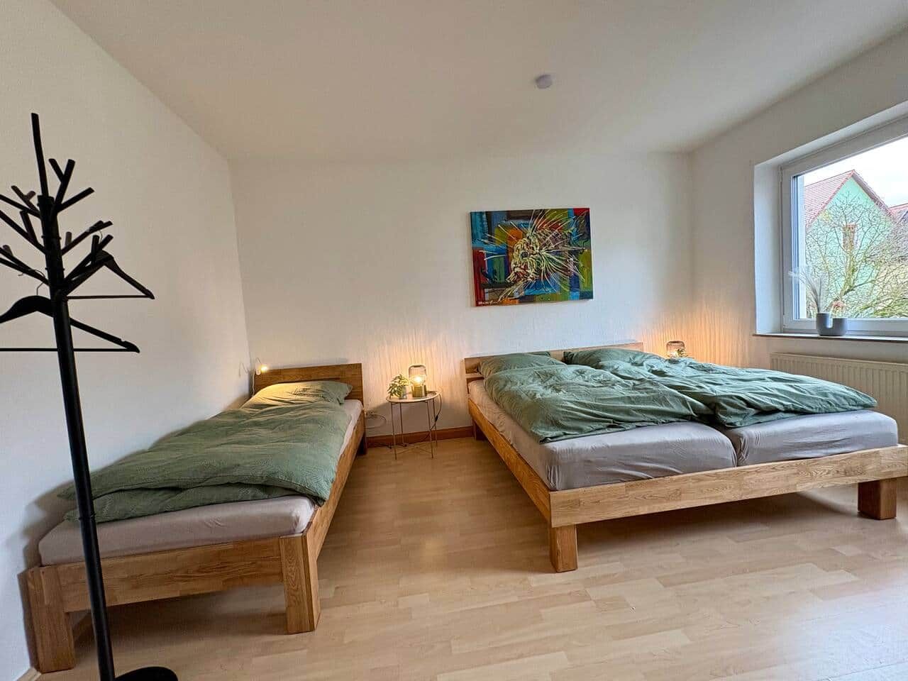Una stanza con due letti di legno, una lampada da terra, un tavolino con lampada e un quadro colorato appeso al muro.