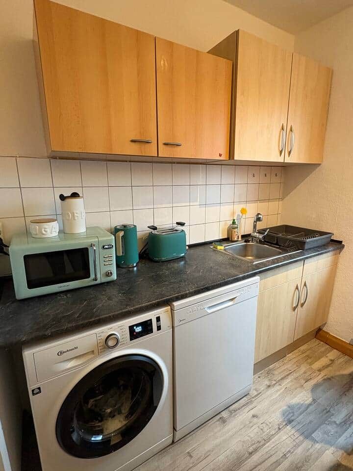A compact kitchen with wooden cabinets, a microwave, a toaster, and a dishwasher.