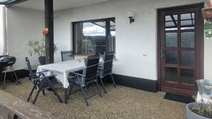 En overdækket terrasse med bord og stole, grill og en potteplante.