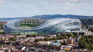 A stadium with a unique curved roof structure, surrounded by residential buildings and a train track. - 🏈 American College Football Fans - 2027 Aer Lingus College Football Classic 🏈 (Dublin)