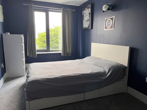 Ein Schlafzimmer mit Bett, einem Fenster mit Vorhängen, einem Heizkörper und Wanddekorationen.