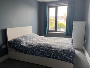 A bedroom with a bed, a window with curtains, and a radiator.