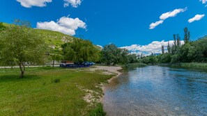 Eine Flussbank mit einer grünen Wiese, Bäumen und blauem Himmel.