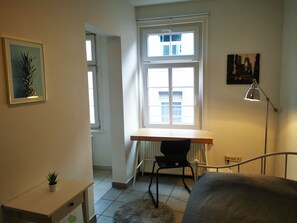 Une petite pièce bien éclairée, avec un bureau, une chaise et un lit.