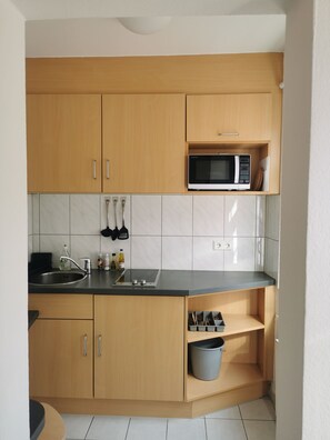 Une petite cuisine avec des meubles de rangement en bois, un four à micro-ondes, un évier et un plan de travail.