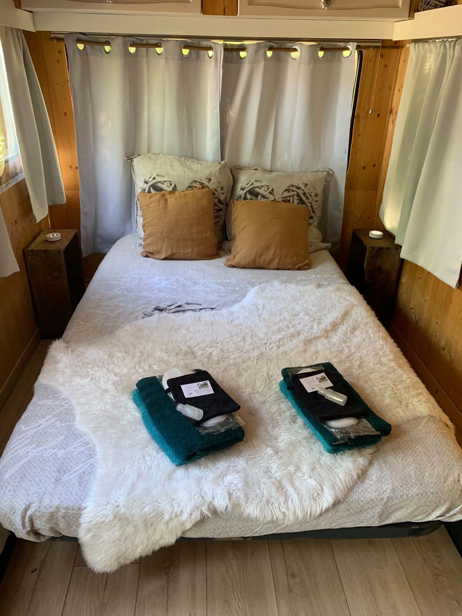 A bed with a white furry cover, two teal towels, and two brown pillows.