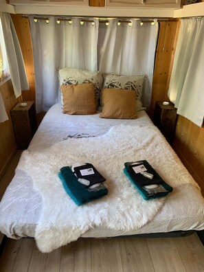 Cama com manta branca felpuda, duas toalhas verde-água e dois travesseiros castanhos.