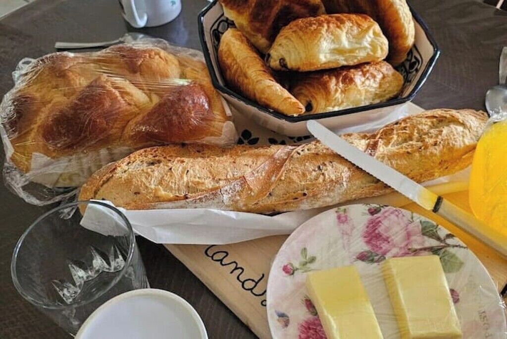 Une table avec divers produits de boulangerie, notamment des croissants et du pain, une assiette avec du beurre et un verre.