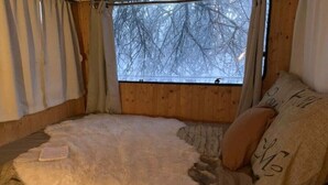 Una habitación acogedora con un ventanal grande, una cama cubierta de piel sintética y vistas a un paisaje nevado.