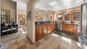 A spacious kitchen with wooden cabinets, a stainless steel refrigerator, and a large window providing natural light. - Elevated Tahoe Escape (Incline Village)
