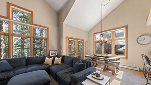 A spacious living room with a sectional sofa, a dining table, and large windows offering a view of trees. - Elevated Tahoe Escape (Incline Village)