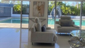 A modern living room with a large glass table, two sofas, and a ceiling fan. - Waterfront retreat with jetty, pool, waterslide and luxury comfort. (Mermaid Waters)