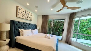A large bed with a tufted headboard, two bedside lamps, and a framed floral artwork on the wall. - Waterfront retreat with jetty, pool, waterslide and luxury comfort. (Mermaid Waters)