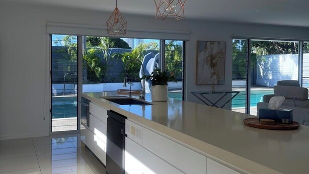 A modern kitchen with a large island, built-in dishwasher, and a view of a swimming pool. - Waterfront retreat with jetty, pool, waterslide and luxury comfort. (Mermaid Waters)