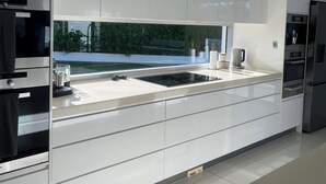 A modern kitchen with white cabinetry, a large island, and built-in appliances. - Waterfront retreat with jetty, pool, waterslide and luxury comfort. (Mermaid Waters)