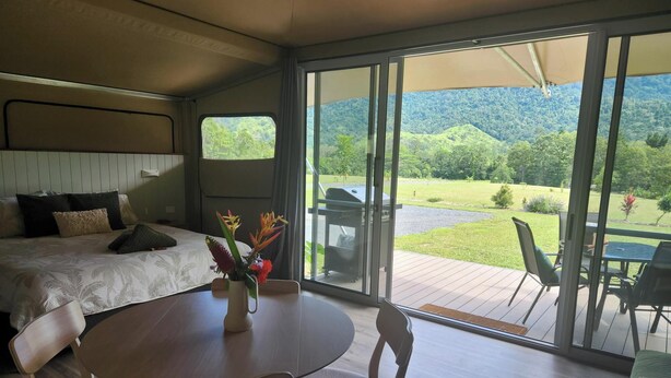 A bedroom with a bed, bedside table, and a view of a deck with outdoor furniture. - Finch Falls Retreat (Finch Hatton)