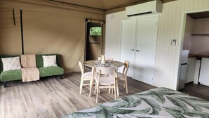 A tented room with a bed, a round table with chairs, a sofa with cushions, and a wardrobe. - Finch Falls Retreat (Finch Hatton)
