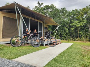Alojamiento en tiendas de campaña con bicicletas estacionadas afuera, un camino de hormigón que conduce a la entrada y un paisaje natural y boscoso de fondo.
