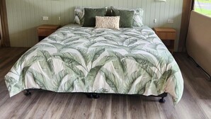 A bed with a tropical leaf pattern bedspread, two bedside tables, and a headboard with built-in lighting. - Finch Falls Retreat (Finch Hatton)