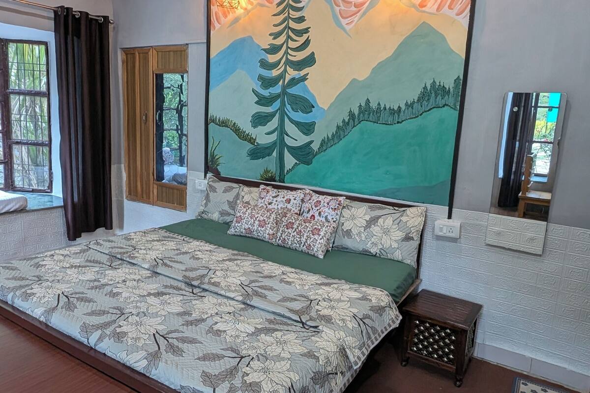 A bedroom with a bed, a bench, a painting of a mountain landscape, and two wall-mounted light fixtures.