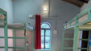 Een slaapzaal met stapelbedden, een rood tapijt, een raam met uitzicht en een plafondlamp.