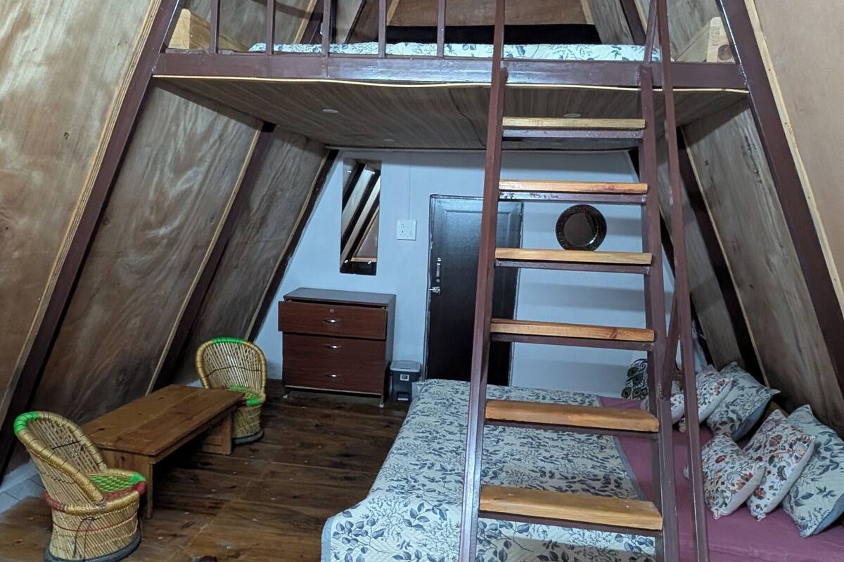 A cozy attic bedroom with a wooden ladder, a small desk, a chair, and a bed with patterned bedding.