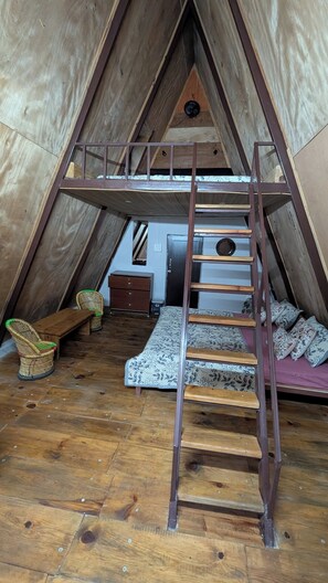 A cozy attic bedroom with a wooden ladder, a small desk, a chair, and a bed with patterned bedding. - Resort Blue Lotus (Ranikhet)
