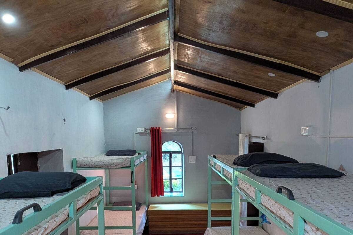 A dormitory room with bunk beds, a red carpet, and a window with a red curtain.