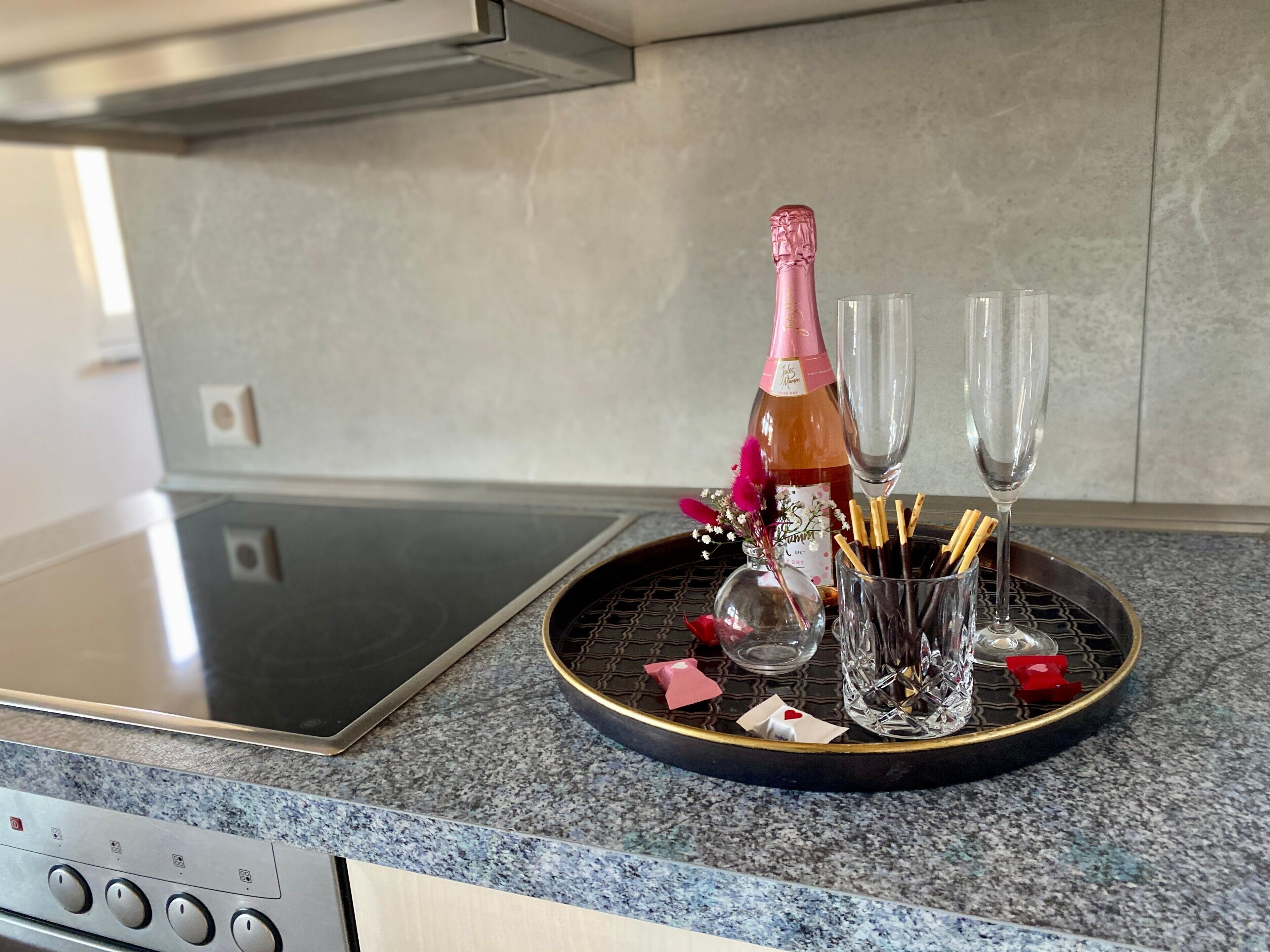 Un comptoir de cuisine avec une bouteille de champagne, deux verres, un vase rempli de fleurs et un plateau contenant divers objets.