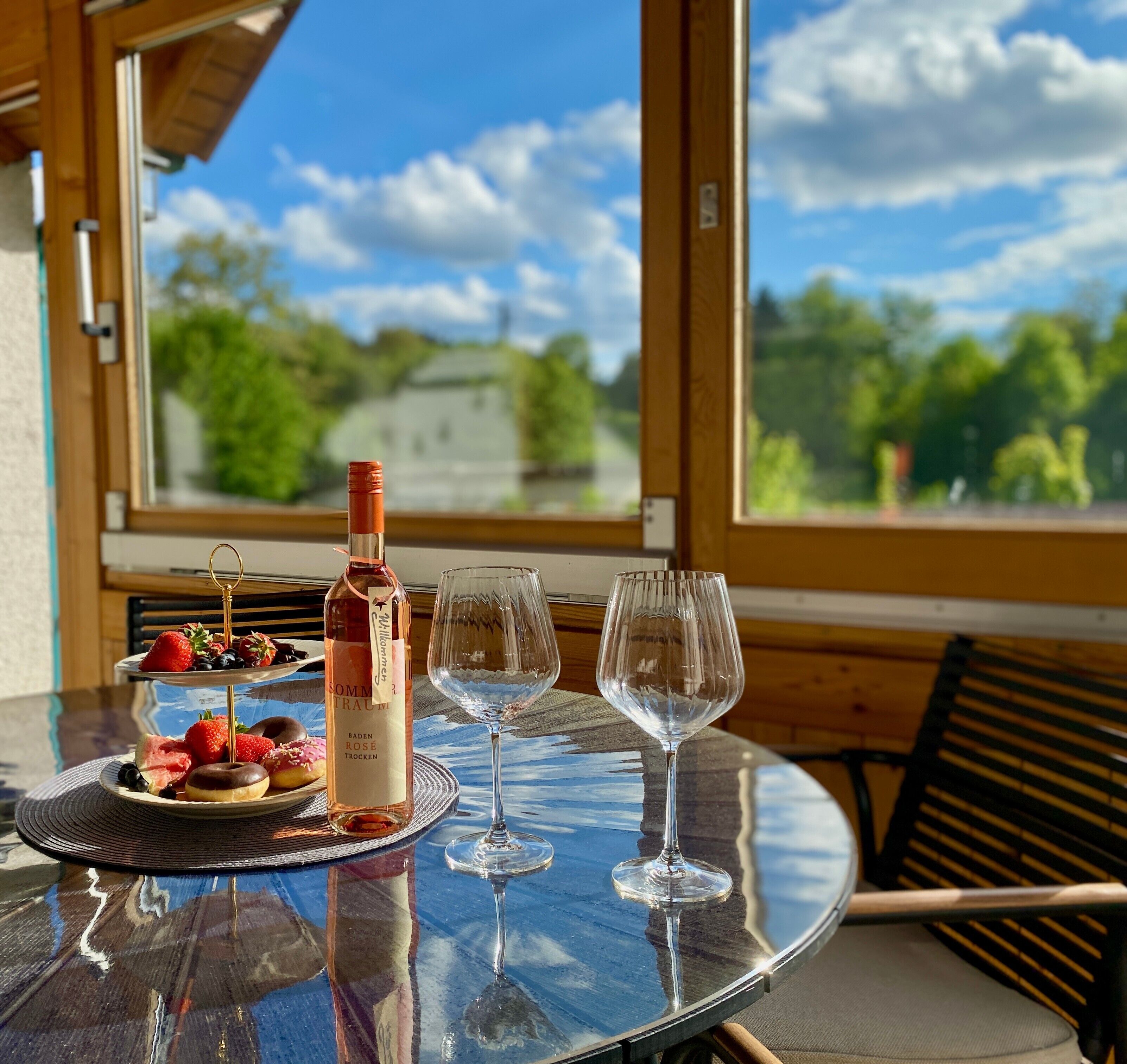 Een tafel met een fles wijn, twee glazen en een bord aardbeien en chocolade.