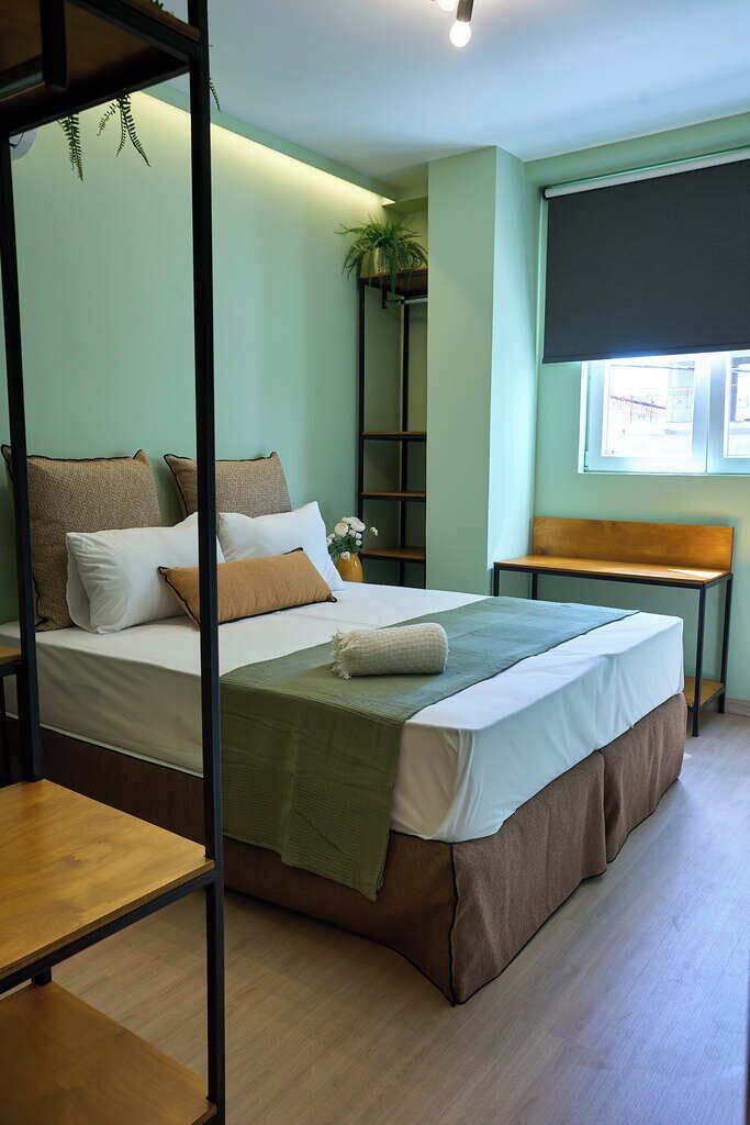 Una habitación con cama, un banco de madera, una mesita y una planta.